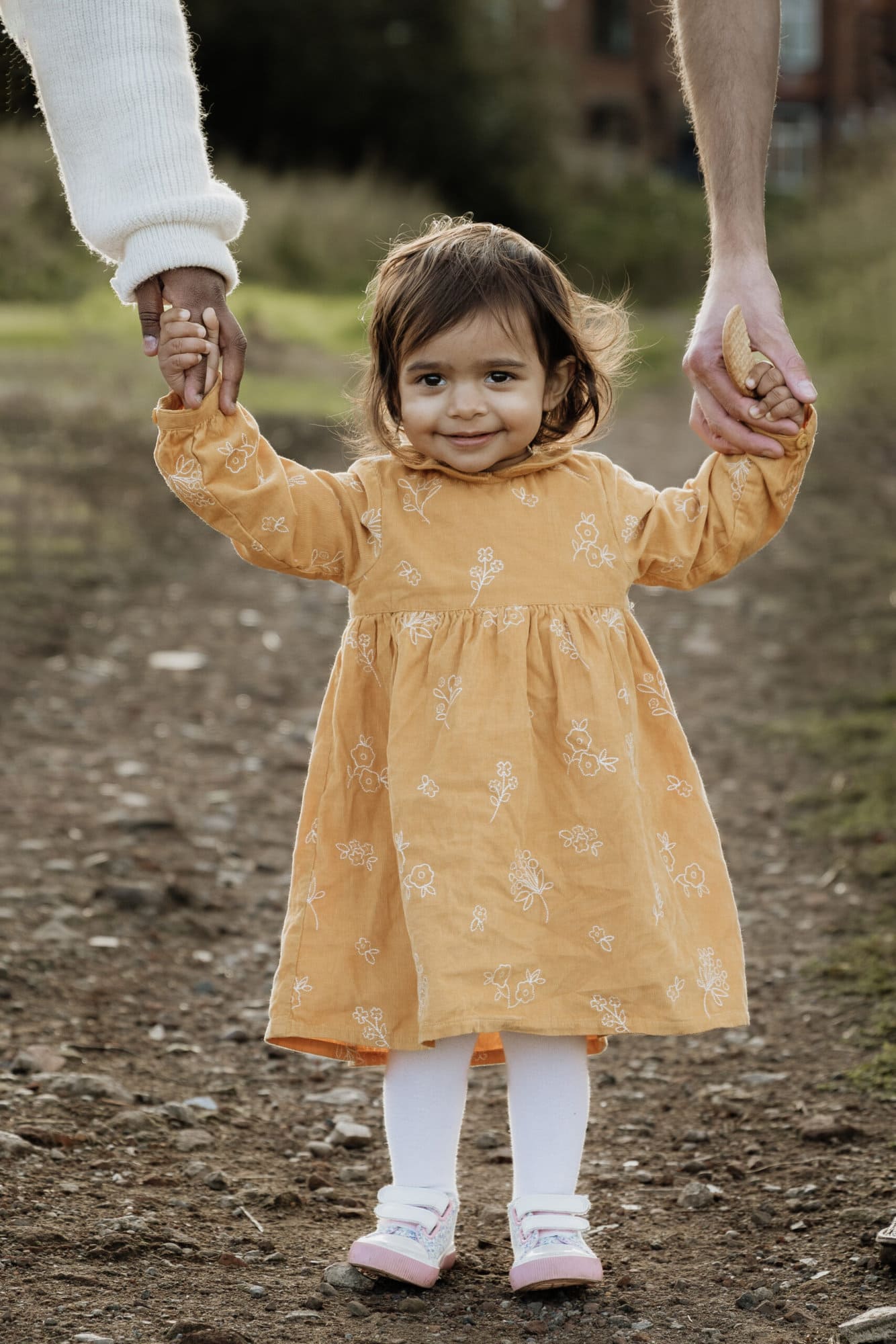 baby girl smiling holding her mother and fathers hands at a family photoshoot in leeds